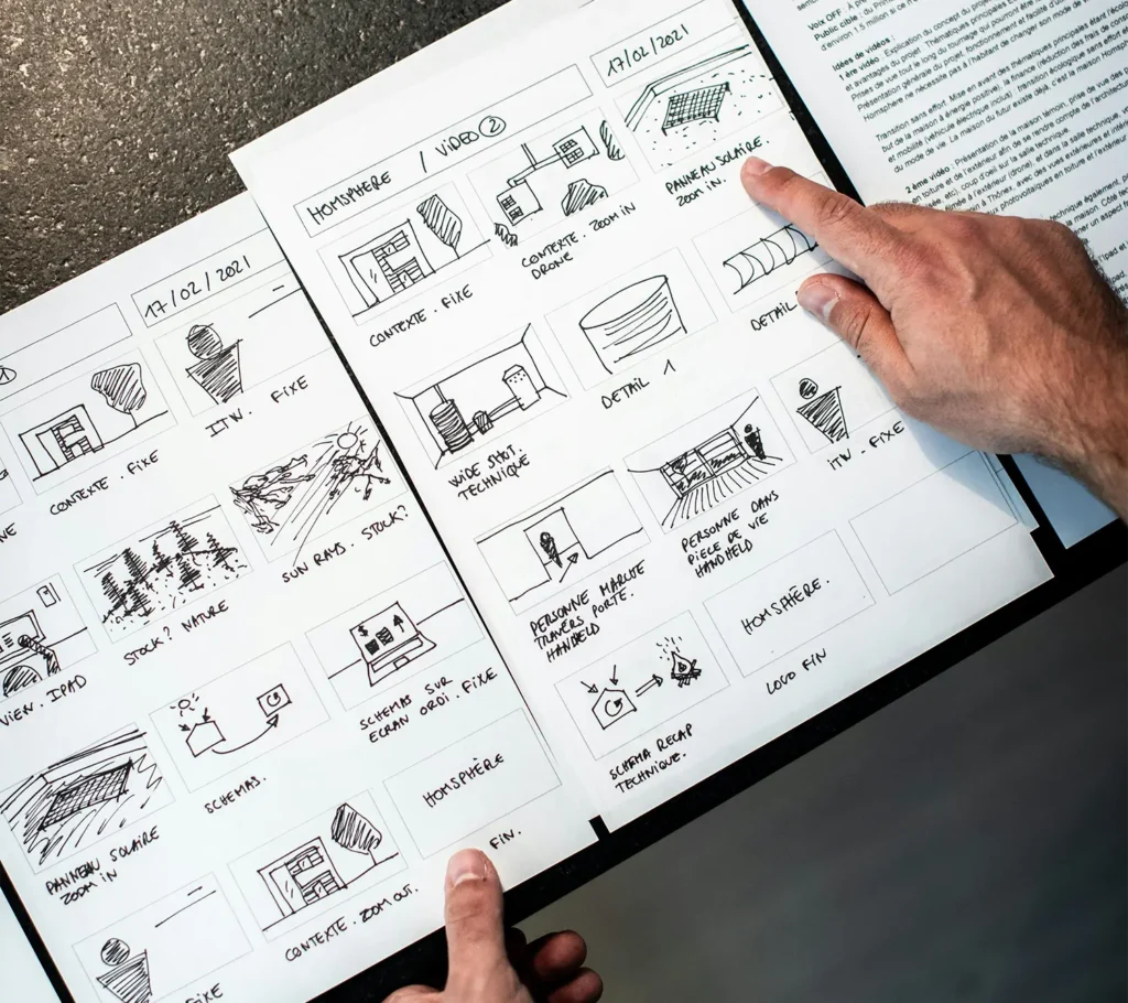 Storyboard dibujado a mano extendido sobre una mesa, con un dedo señalando viñetas y luz lateral creando sombras suaves.